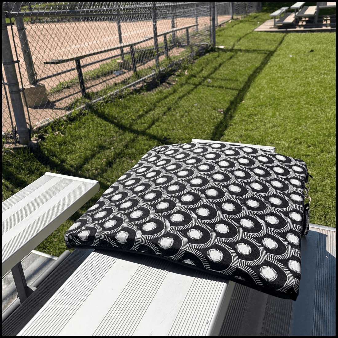 a stylish seat cushion with a black and white geometric pattern on a metal bleacher at an outdoor baseball diamond