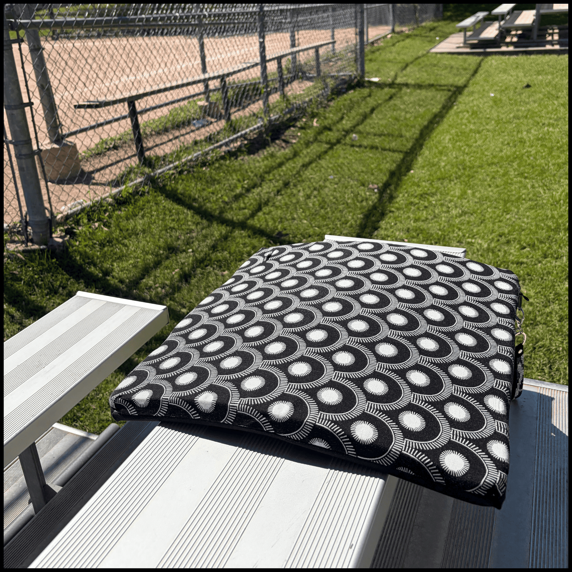a stylish seat cushion with a black and white geometric pattern on a metal bleacher at an outdoor baseball diamond